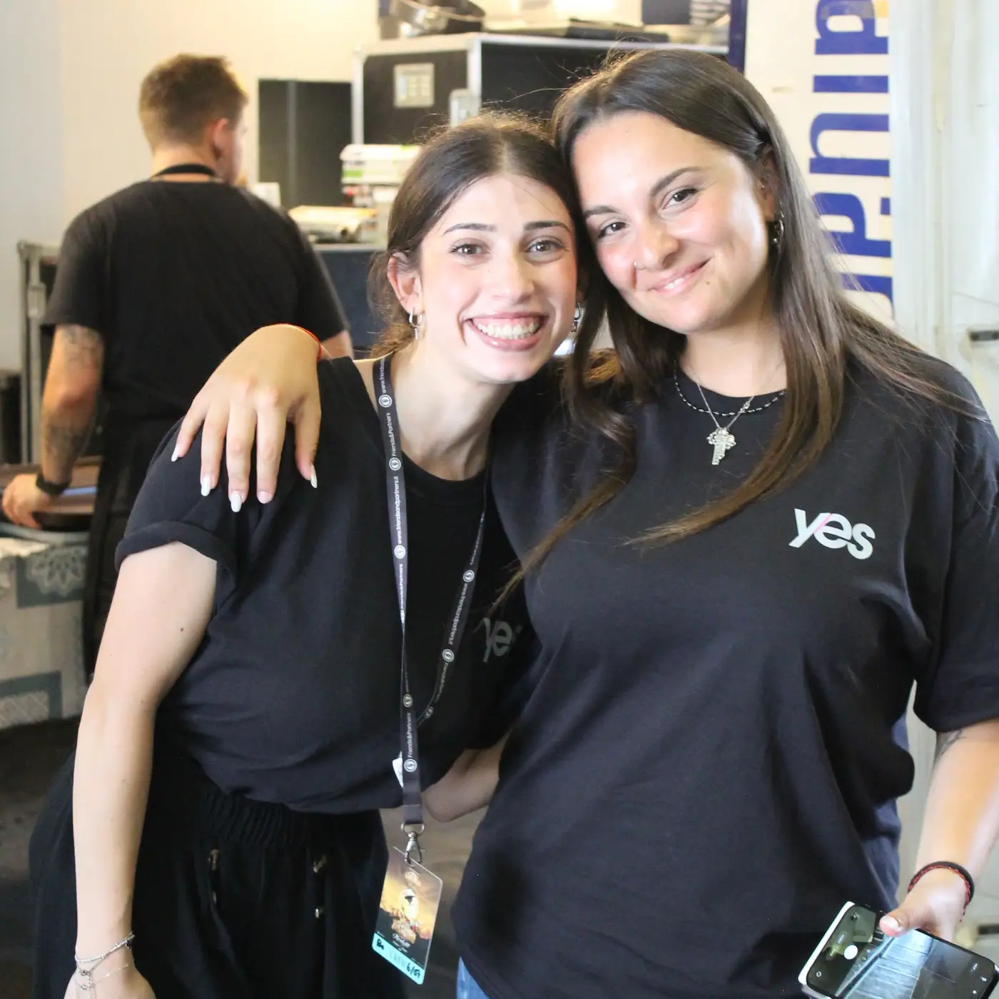 Due giovani collaboratrici YES con la maglia aziendale sorridono abbracciate nel backstage di un evento