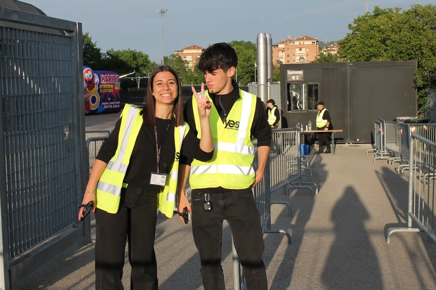 Due giovani steward YES in pettorina gialla sorridono al varco d'ingresso