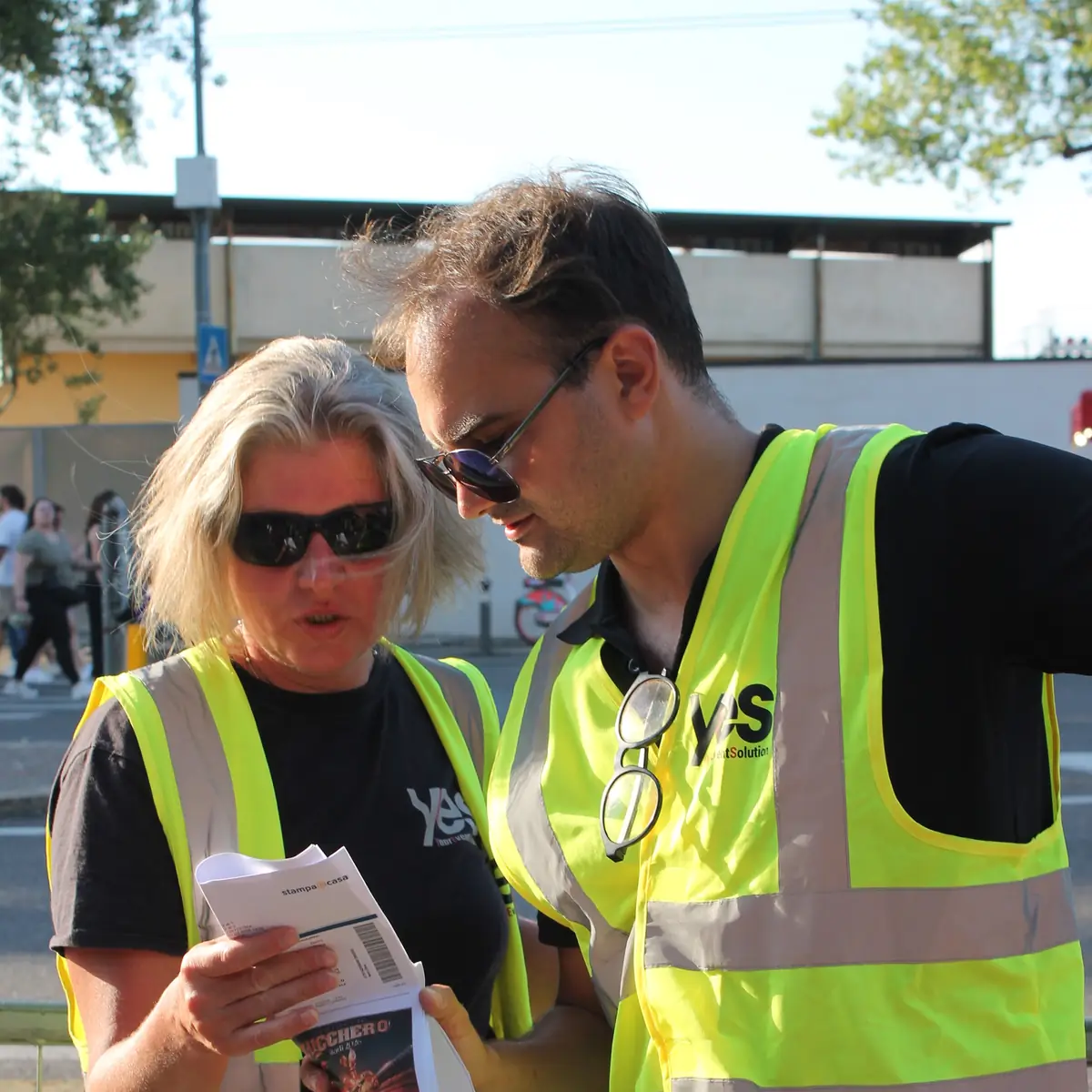 Due operatori YES in pettorina leggono insieme il foglio del servizio all'ingresso dell'evento