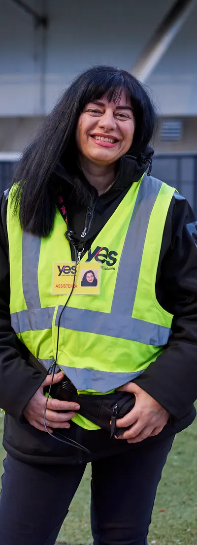 Operatrice YES con la pettorina gialla e il pass sorride sul prato di uno stadio